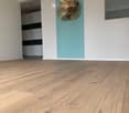 Empty room with light wooden flooring, white walls, and a decorative gold flower wall piece. A closet with black and white doors is visible in the background.