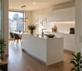 Modern kitchen with white cabinetry, island, pendant lights, and a view of the city through large windows. Includes a coffee maker, chairs, and plants.