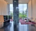 Modern lobby area with a black polished floor, a large central marble pillar, and a seating area with a sofa, chairs, and a glass coffee table.