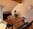 Bright, modern living space with wooden floors, a large window offering a scenic view, a sofa, a dining table with chairs, an armchair, and decorative lamps.