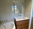 Modern bathroom with a white bathtub, wooden sink cabinet, and a large mirror above the sink.
