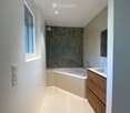Modern bathroom with a bathtub, sink, and wooden cabinet. Features a large window and sleek, contemporary design.