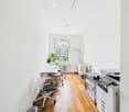 empty office with light wooden floor, white walls, white office furniture, and one desk by the window