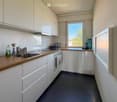 Modern kitchen with white cabinets, wooden countertops, and stainless steel appliances. Features a sink, oven, and various small items on the counter.