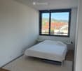 Minimalist bedroom with a white bed, nightstands, table lamps, and a large window overlooking a cityscape.