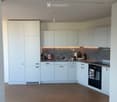 Modern kitchen with white cabinets, wooden herringbone flooring, and a granite backsplash. Features a sink, oven, and various small items on the counter.