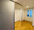 Empty room with wooden flooring, white walls, and a large mirrored wardrobe. A door with a window leads to another space.