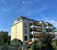 Modern multi-story residential building with balconies, large windows, and surrounding greenery.