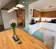 Bright, modern kitchen and dining area with white and light wood cabinets, a wooden dining table with chairs, a vase of pink tulips, and various kitchen appliances including a coffee maker and blender.