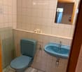 A small bathroom with a blue toilet, a matching blue sink, a mirror, and a glass shower enclosure. Toilet paper is placed on a shelf above the toilet.