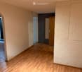 Empty hallway with wooden flooring, beige walls, and recessed ceiling lights. Features an arched doorway and a textured wall section.