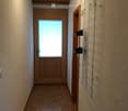 Empty hallway with wooden flooring, a wooden door with frosted glass panel, and a metal coat rack on the right wall.