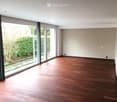 Empty room with wooden flooring, large glass sliding doors leading to a garden, and white walls.
