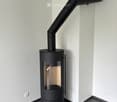 Modern black wood-burning stove with a sleek design, mounted on a dark grey tiled floor against white walls.
