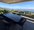 Balcony with a panoramic view of a valley and lake, featuring a table and chairs.