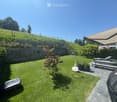 Well-maintained garden with a lawn, a small tree, potted plants, outdoor furniture including a bench and a table, and a covered patio area.