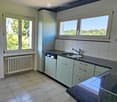 Modern kitchen with light grey cabinets, tiled floor, and a large window overlooking greenery. Features a sink, faucet, and dishwasher.