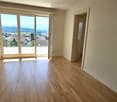 Empty room with wooden flooring, large sliding glass door leading to a balcony, radiator on the left side, and a doorway on the right.