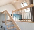 Modern wooden staircase with metal balustrade, leading to an upper level with a skylight window and a view of a room below.