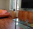 Modern living room with wooden flooring, a glass coffee table, a leather sofa, a TV stand, and a small plant on the windowsill.