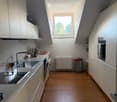 Modern kitchen with white cabinets, wooden flooring, stainless steel appliances, and a large window letting in natural light.
