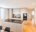 Modern kitchen with white cabinets, black countertops, a central island, and a dining area with a wooden table and black chairs.