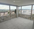 Modern balcony with grey tiled floor, metal railing, and scenic view of surrounding buildings and landscape.