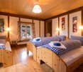 Cozy wooden bedroom with two single beds, checkered bedding, wooden floor, and warm lighting.