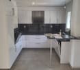 Modern kitchen with white cabinets, stainless steel appliances, and a black countertop. Features an island with a stool and various items on the counter.