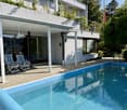 Modern house with a swimming pool, lounge chairs, and a covered patio area.