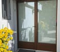Balcony with a wooden sliding door, a doormat, and a potted plant with yellow flowers.