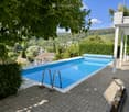 Outdoor area with a rectangular swimming pool surrounded by a tiled deck, featuring a scenic view of a valley and trees.