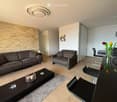 Modern living and dining area with a grey sofa, armchair, coffee table, dining table, chairs, and a vase with flowers on the counter.