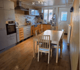 Modern kitchen with light wood flooring, white cabinets, stainless steel appliances, and a dining area with a table and chairs.