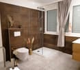 Modern bathroom with brown tiles, a glass-enclosed shower, a toilet, a sink, and decorative elements including a vase with dried plants and a framed picture on the wall.