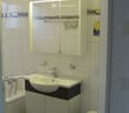 Modern bathroom with white tiles, a sink with a mirror cabinet, a toilet, and a bathtub. The mirror has built-in lighting, and the walls feature decorative tiles near the top.