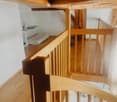 Wooden staircase with a handrail and a small shelf on the landing, leading to a lower level with tiled flooring.