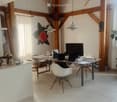 Open-plan living and dining area with exposed wooden beams, modern furniture, and a large screen. Includes a dining table with chairs, laptops, and decorative items.