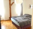 Cozy bedroom with wooden flooring, a large bed with dark bedding, a round pendant light, and a picture frame on the wall.