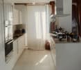 Modern kitchen with white cabinets, stainless steel appliances, and a large island. Features include a built-in oven, a blender, and various kitchen utensils on the counter.