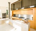 Modern kitchen with light wood cabinets, stainless steel appliances, island, and various kitchen items on the counter.