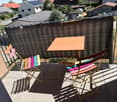 Balcony with a table and colorful folding chairs, surrounded by a metal railing and a privacy screen, overlooking a residential area.