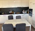 Modern kitchen with white cabinets, stainless steel appliances, a white dining table with four grey chairs, and various kitchen items on the counter.