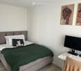 A modern bedroom with a neatly made bed, a desk with a laptop, and two framed pictures on the wall.