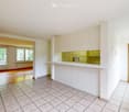 Empty room with tiled floor, wooden door, and a small kitchen area with cabinets and a countertop.