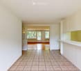 Empty hallway with tiled floor and white walls, leading to an open living space with wooden flooring and large windows.