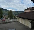View from a rooftop showing a parking area with several cars, a garage, and a scenic mountain view in the background.