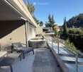 Balcony with tiled floor, modern furniture including a chair, table, and a hot tub, overlooking a scenic view of trees and hills.