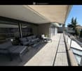 Modern balcony with grey sofa, coffee table, and chairs, featuring a retractable awning and a view of the surrounding area.