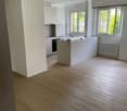 Modern kitchen with white cabinets, a central island, and wooden flooring. Features include large windows, a radiator, and a built-in oven.
